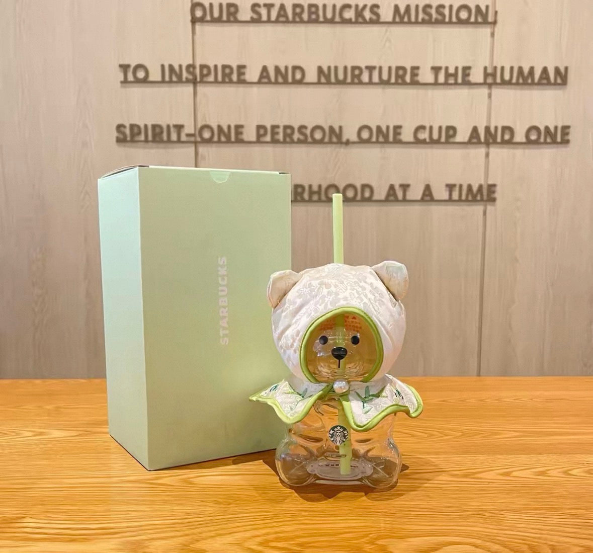 Cute bear-shaped glass tumbler with a straw, featuring a clear design and a soft green lid. Comes with a matching embroidered fabric cover. Perfect for cold drinks and easy to clean.