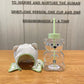 Cute bear-shaped glass tumbler with a straw, featuring a clear design and a soft green lid. Comes with a matching embroidered fabric cover. Perfect for cold drinks and easy to clean.
