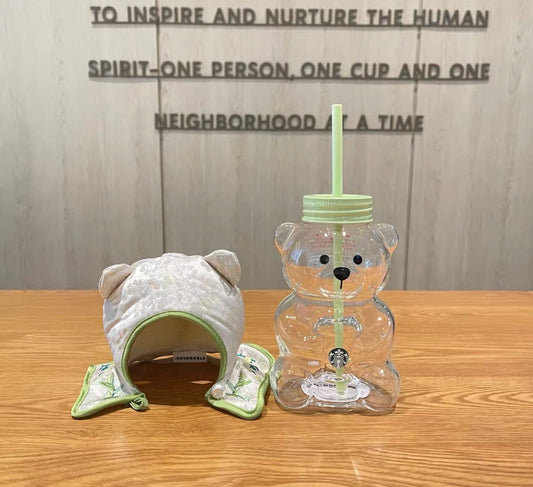 Cute bear-shaped glass tumbler with a straw, featuring a clear design and a soft green lid. Comes with a matching embroidered fabric cover. Perfect for cold drinks and easy to clean.